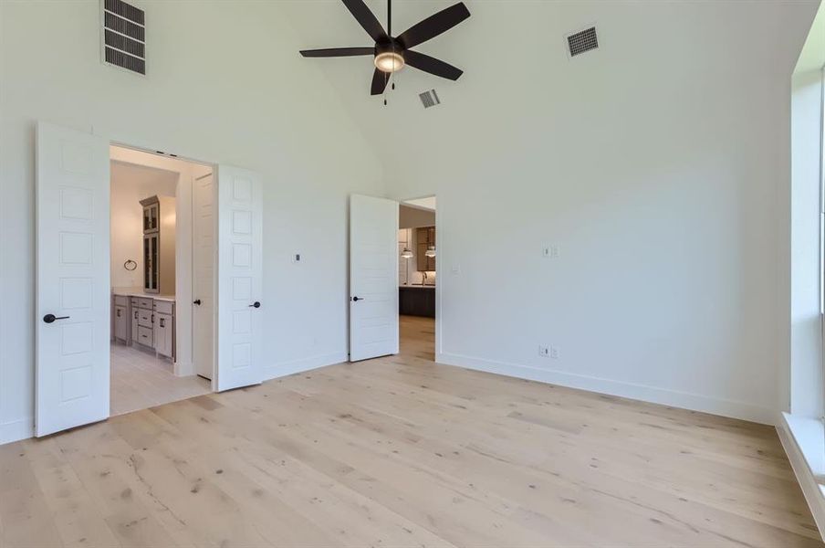 Unfurnished bedroom with high vaulted ceiling, light wood-type flooring, connected bathroom, and ceiling fan