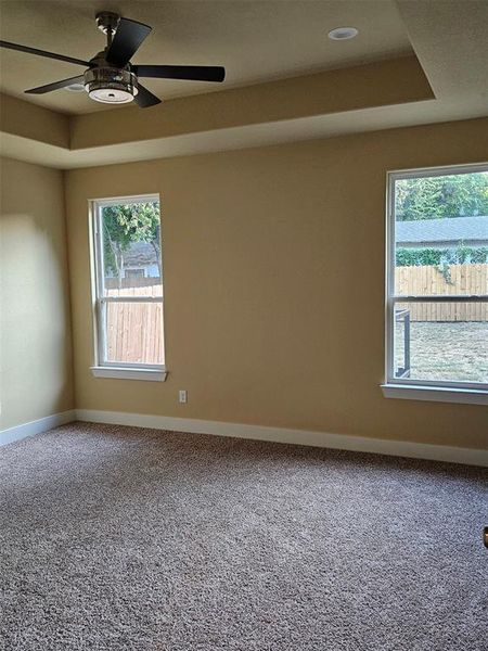 Carpeted empty room with ceiling fan and a raised ceiling