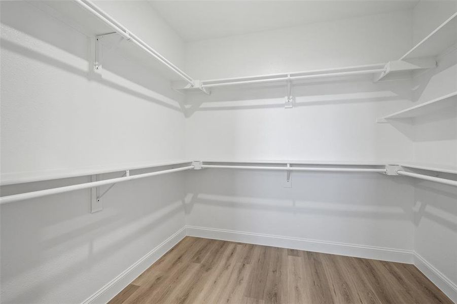 Spacious walk-in closet featuring white wire shelving, multiple hanging rods, corner shelving units, and wood-finish flooring Spacious walk-in closet featuring white wire shelving, multiple hanging rods, corner shelving units, and wood-finish flooring