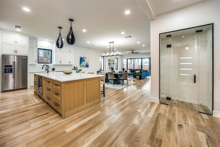 Kitchen featuring a large island, sink, stainless steel refrigerator with ice dispenser, decorative light fixtures, and white cabinets