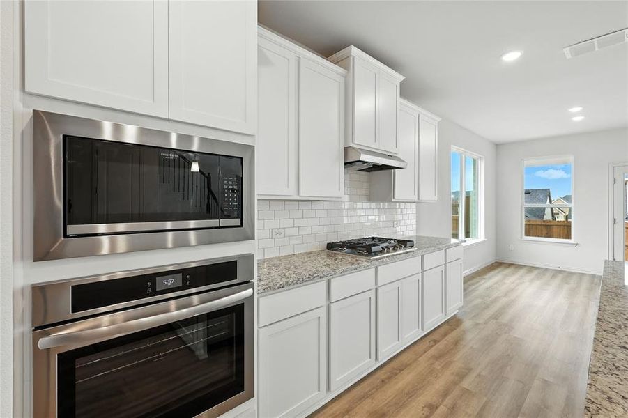 Kitchen featuring stainless steel appliances, light stone counters, white cabinetry, decorative backsplash, and light wood finished floors Kitchen featuring stainless steel appliances, light stone counters, white cabinetry, decorative backsplash, and light wood finished floors