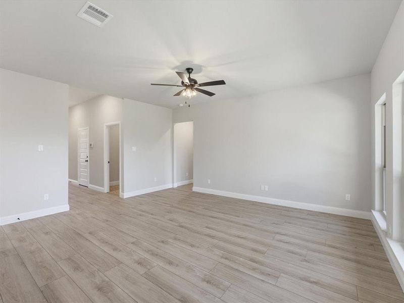 Spacious living room featuring light wood-finish flooring, a contemporary ceiling fan, and light-toned walls Spacious living room featuring light wood-finish flooring, a contemporary ceiling fan, and light-toned walls