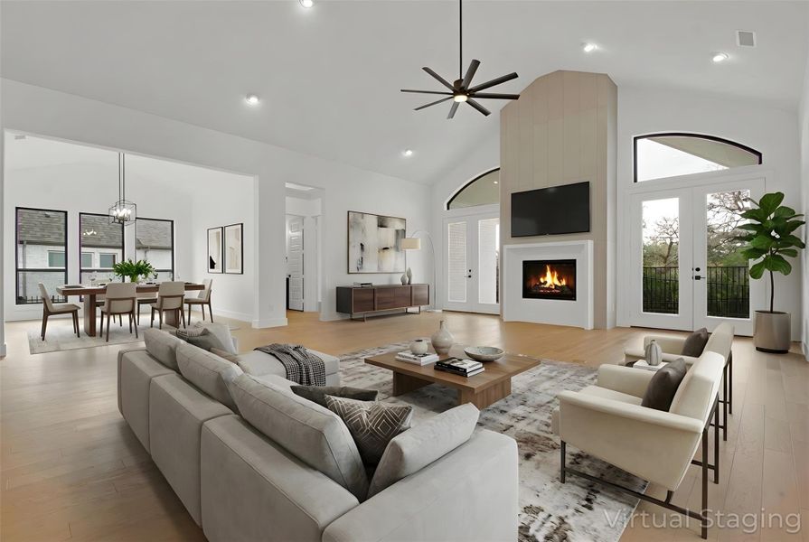 Virtually-Staged open-concept Great Room featuring 16ft vaulted ceiling, a gas fireplace, light hardwood floors, a ceiling fan, and double french doors to outdoor patio with scenic, greenbelt view