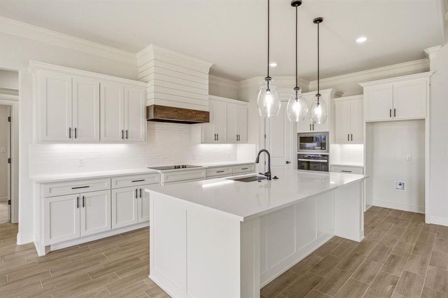Kitchen with white cabinetry, backsplash, wood tiled floors, a kitchen island with sink, and stainless steel appliances