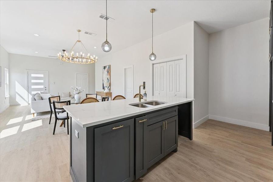 Kitchen with light stone countertops, pendant lighting, a kitchen island with sink, light wood-style floors, and open floor plan