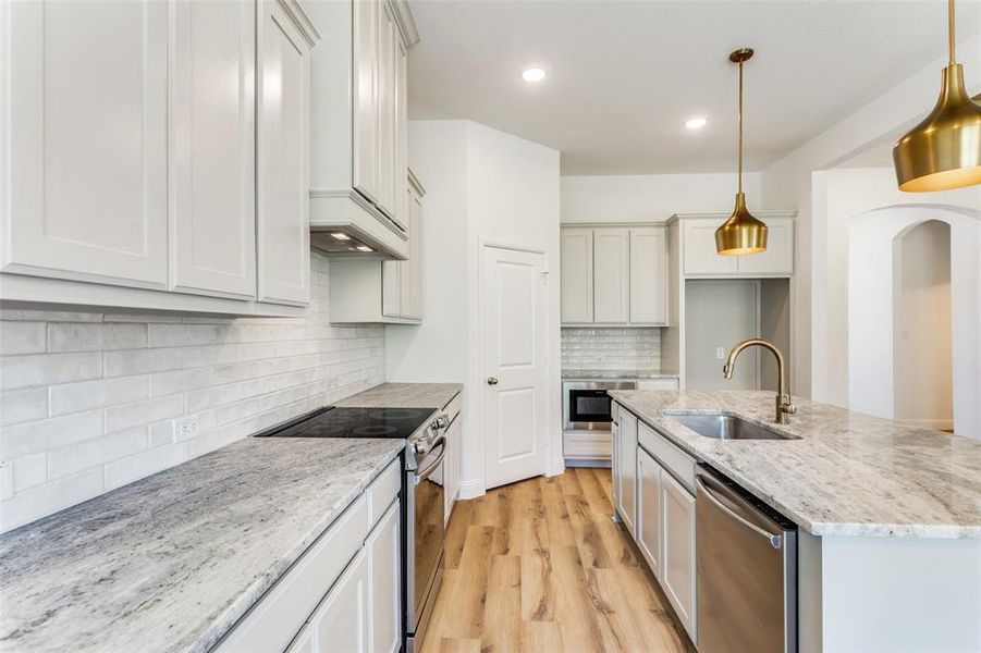 Kitchen featuring decorative light fixtures, light hardwood / wood-style floors, stainless steel appliances, backsplash, and sink