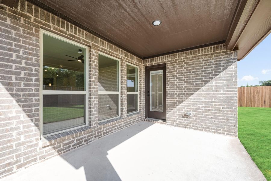 Covered back patio with concrete floor, brick exterior, large windows, and door leading inside with fenced yard beyond.