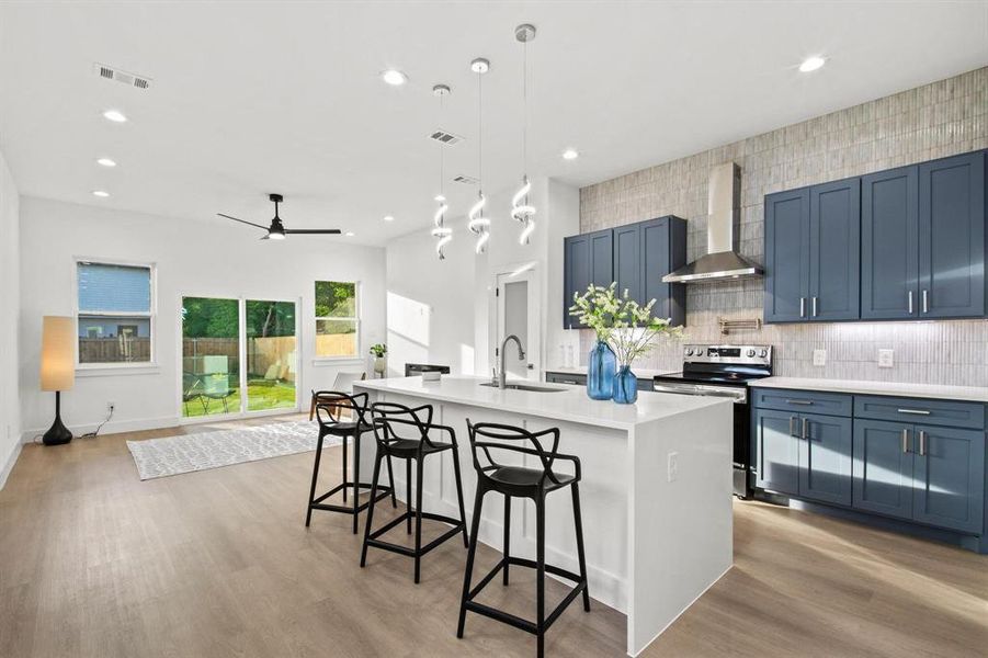 Kitchen with blue cabinetry, tasteful backsplash, a center island with sink, stainless steel electric stove, and a kitchen breakfast bar