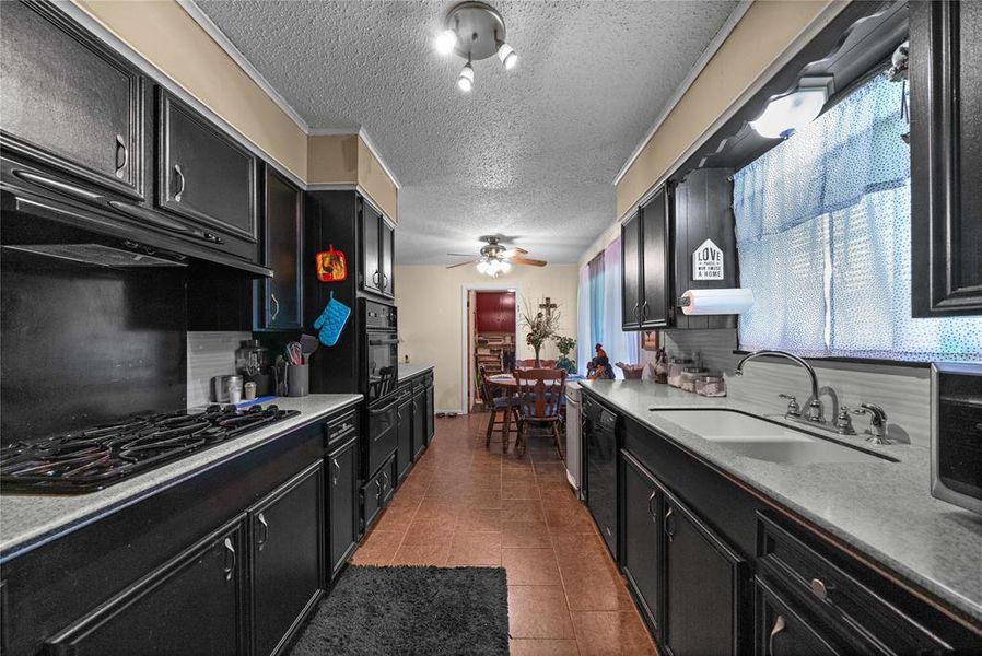 Kitchen with dark cabinetry, black appliances, a textured ceiling, a ceiling fan, and light countertops