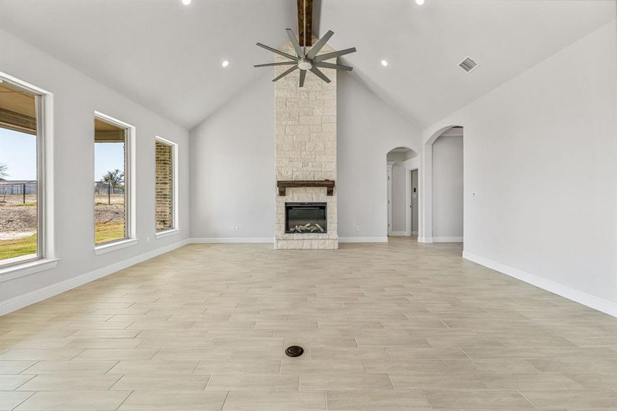 Unfurnished living room featuring beam ceiling, high vaulted ceiling, a fireplace, a ceiling fan, and wood tiled floors