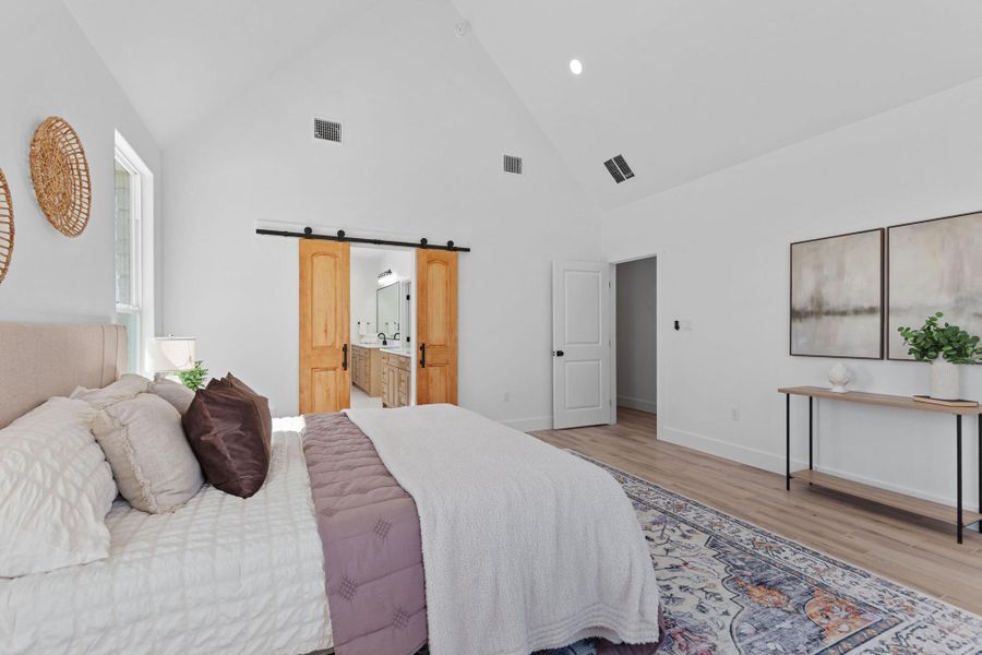Bedroom featuring a barn door, lofted ceiling, ensuite bathroom, light wood finished floors, and recessed lighting Bedroom featuring a barn door, lofted ceiling, ensuite bathroom, light wood finished floors, and recessed lighting