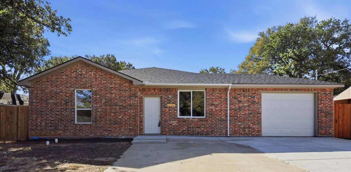 Ranch-style home with a garage, brick siding, a shingled roof, and driveway