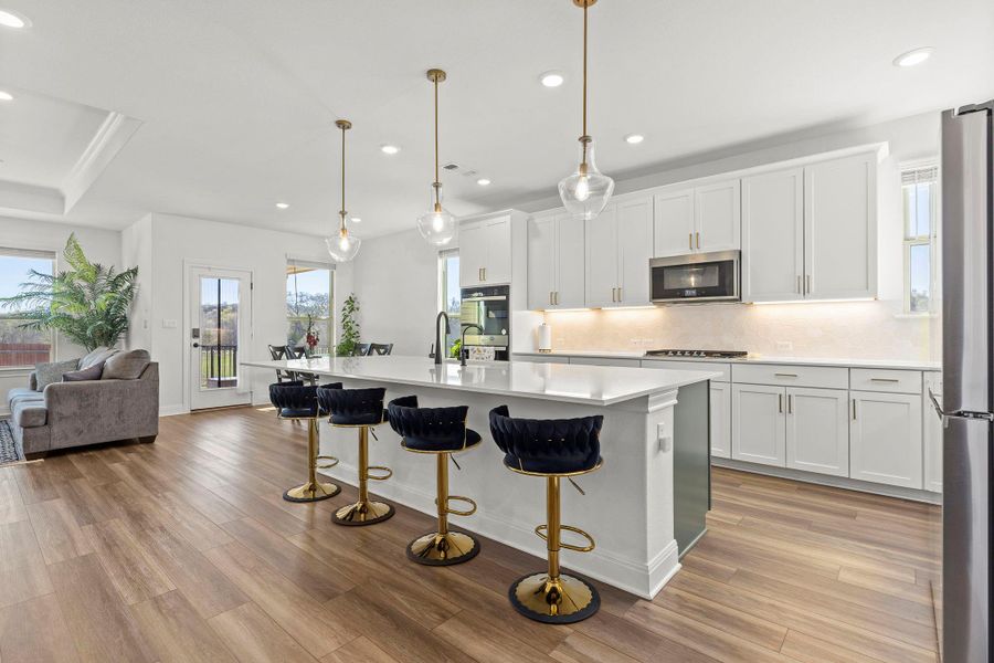 Kitchen with white cabinetry, a breakfast bar area, a center island with sink, open floor plan, and light wood-type flooring