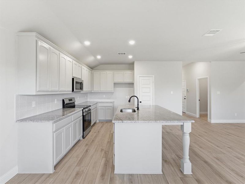 Open-concept kitchen featuring an island with a built-in sink, white cabinetry, granite countertops, and stainless steel appliances Open-concept kitchen featuring an island with a built-in sink, white cabinetry, granite countertops, and stainless steel appliances