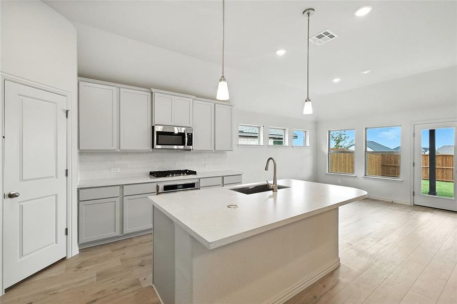 Kitchen with decorative backsplash, light countertops, light wood finished floors, recessed lighting, and a kitchen island with sink Kitchen with decorative backsplash, light countertops, light wood finished floors, recessed lighting, and a kitchen island with sink