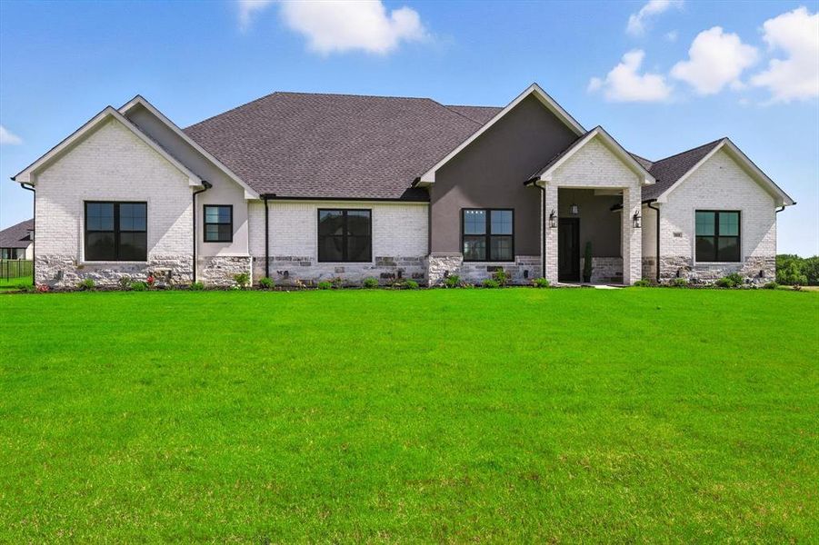 View of front of property featuring a front yard, stone siding, brick siding, and roof with shingles View of front of property featuring a front yard, stone siding, brick siding, and roof with shingles