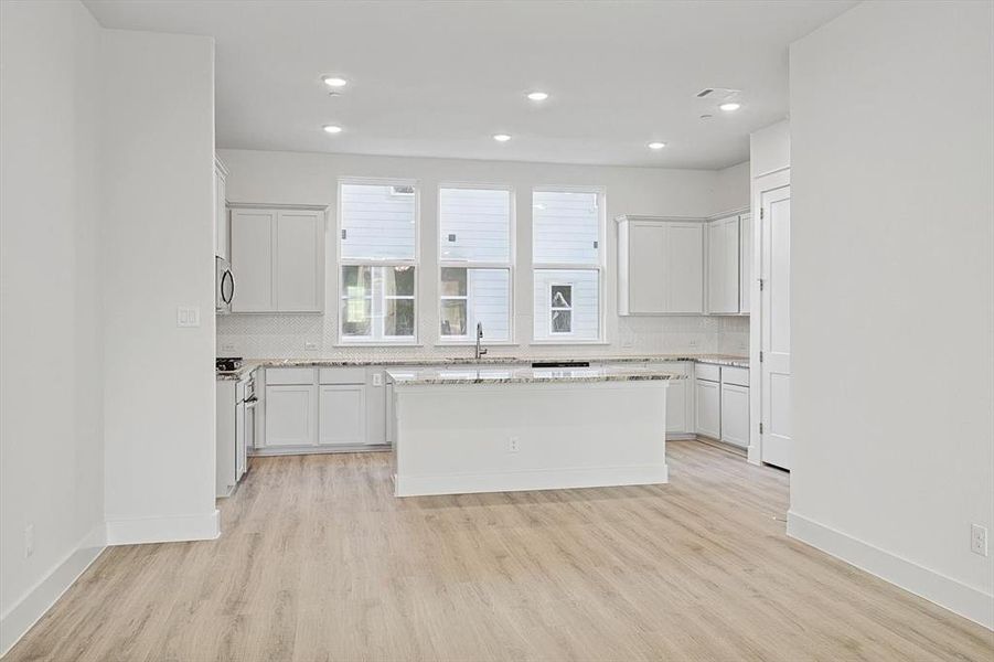 Kitchen featuring a sink, stainless steel microwave, decorative backsplash, and light wood finished floors