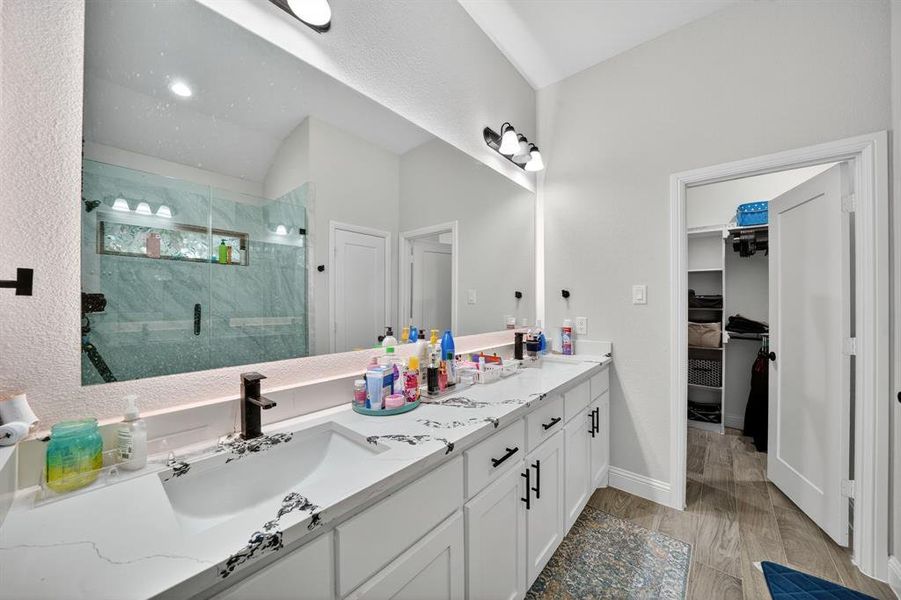 Full bath featuring a marble finish shower, double vanity, dark wood finished floors, and a walk in closet