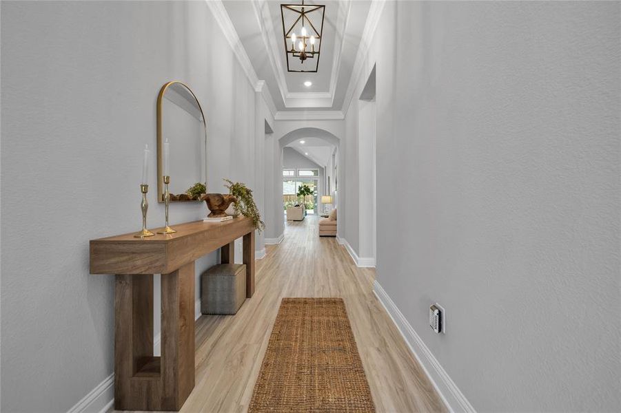 Hall with arched walkways, light wood-type flooring, ornamental molding, a chandelier, and recessed lighting Hall with arched walkways, light wood-type flooring, ornamental molding, a chandelier, and recessed lighting