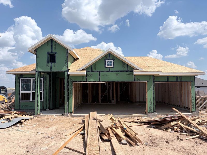 A new home takes shape under a bright sky, showcasing robust framing and gabled rooflines.