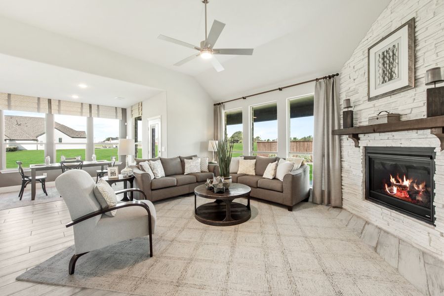 Living room with vaulted ceiling, stone fireplace, gray sofas, and ceiling fan overlooking backyard windows