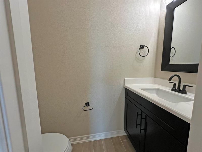 Half bathroom with vanity, a textured wall, and wood finish floors