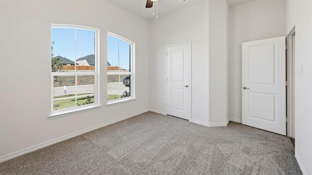 Room featuring two arched windows, neutral-toned carpeting, white panel doors, and a ceiling fan