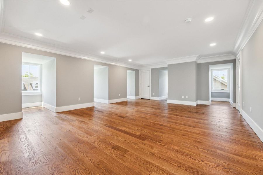 This view of this spacious 3rd floor flex/media/game room features beautiful hardwood floors, soft gray walls, and abundant natural light from multiple windows. The recessed lighting and crown molding add a touch of elegance, perfect for a versatile living space.  There are also 2 large closets.