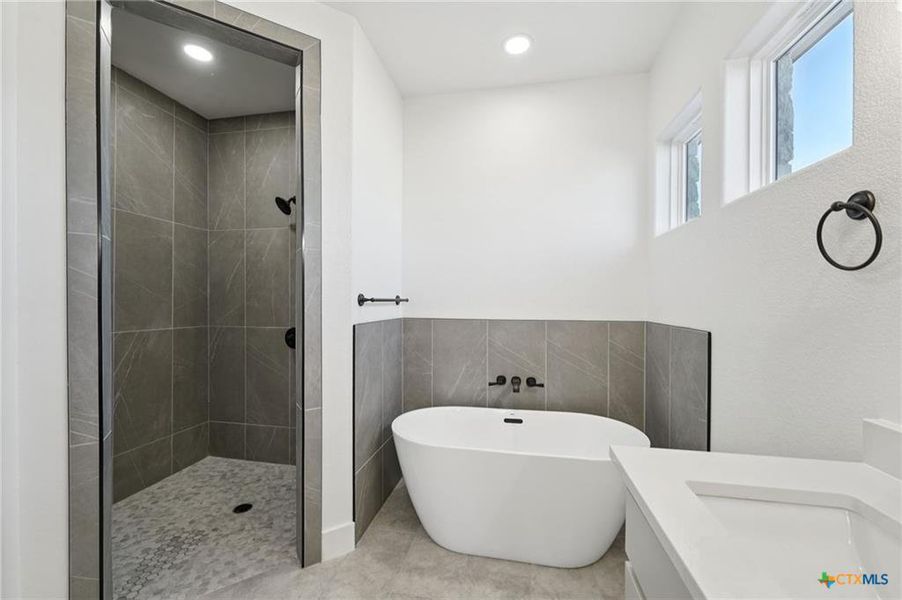 A freestanding soaking tub complements the spacious walk-in shower in this modern primary bath. A freestanding soaking tub complements the spacious walk-in shower in this modern primary bath.