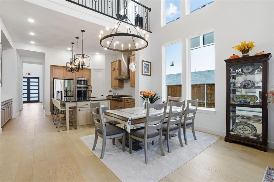 Dining area with light wood-type flooring, a towering ceiling, recessed lighting, and a chandelier Dining area with light wood-type flooring, a towering ceiling, recessed lighting, and a chandelier