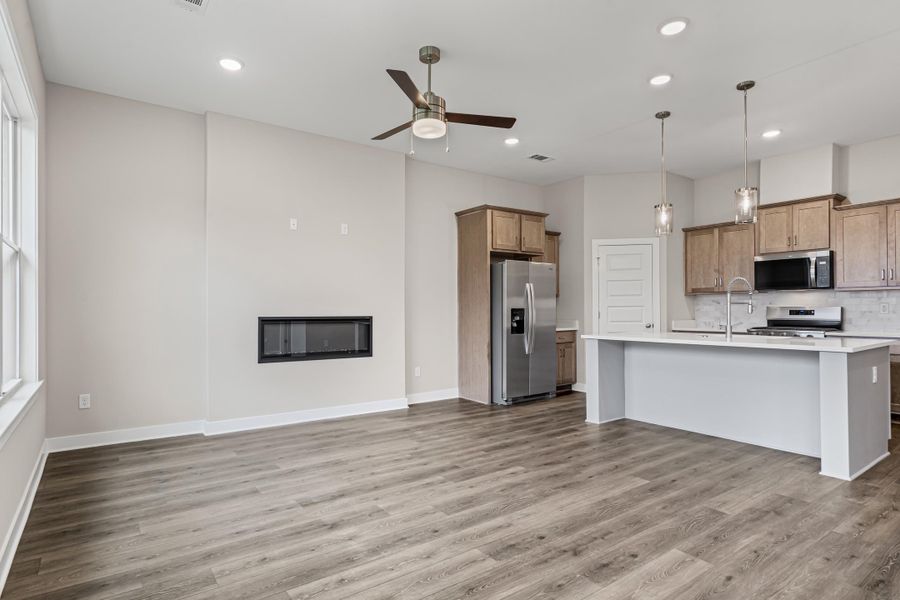 Kitchen featuring stainless steel appliances, decorative backsplash, light wood finished floors, a kitchen island with sink, and open floor plan