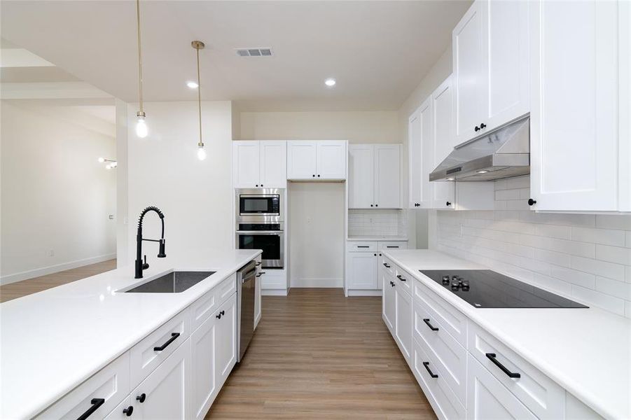 Kitchen with light wood-type flooring, hanging light fixtures, sink, and white cabinetry