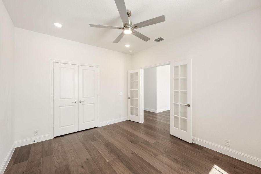 Empty bedroom with dark hardwood floors, ceiling fan, double closet doors, and glass-paned French doors leading to an adjoining room. Empty bedroom with dark hardwood floors, ceiling fan, double closet doors, and glass-paned French doors leading to an adjoining room.
