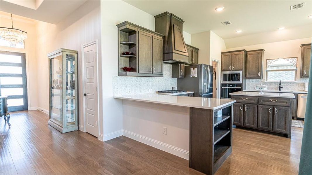 Kitchen featuring wood-finish flooring, custom wood cabinetry, stainless steel appliances, and light-toned countertops