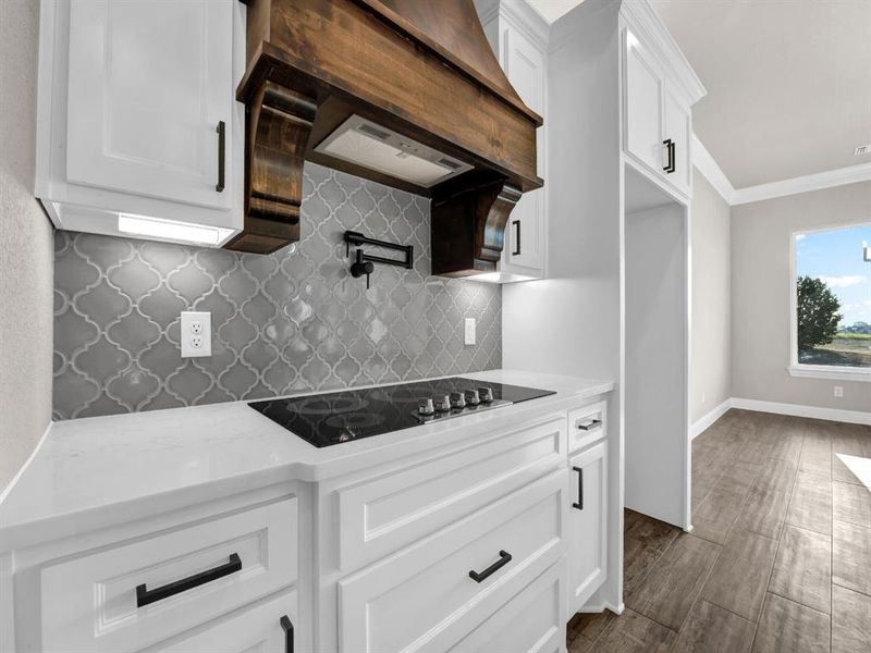 Kitchen with tasteful backsplash, crown molding, black electric cooktop, white cabinetry, and custom range hood