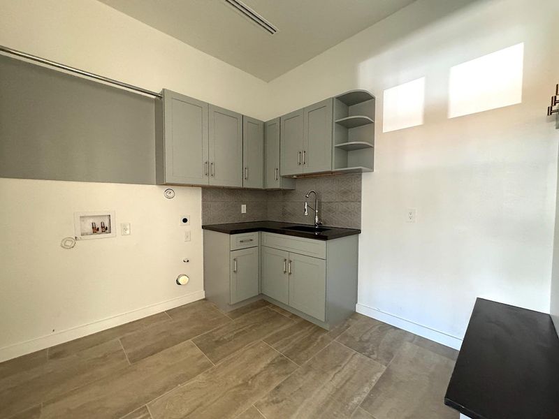 Kitchen with dark countertops, a sink, gray cabinetry, decorative backsplash, and open shelves