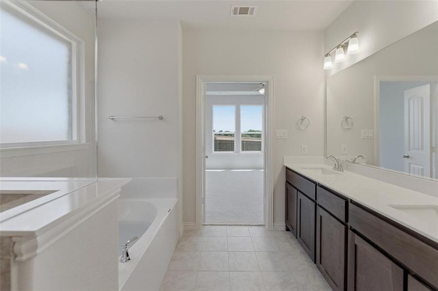 Bathroom featuring a dual vanity with undermount sinks, a built-in bathtub, a frosted window, and tile flooring