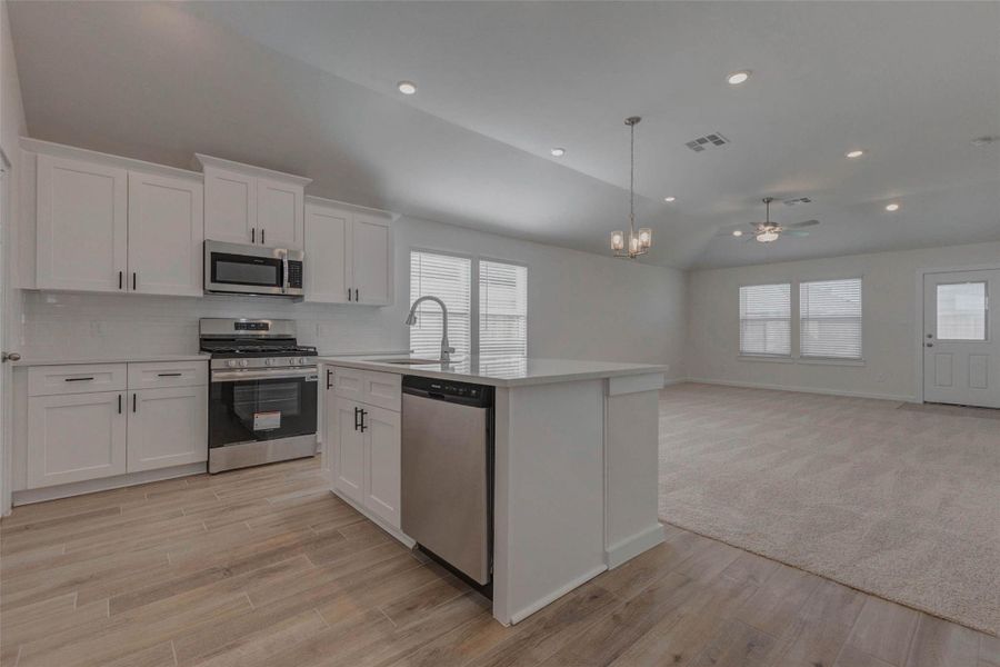 This view perfectly captures the home’s seamless flow between kitchen, dining, and living areas. The vaulted ceiling adds volume while recessed lighting and a modern chandelier create ambiance. Natural wood-look tile and clean white finishes reflect the sunlight pouring in through large windows, making this space ideal for both entertaining and relaxing.