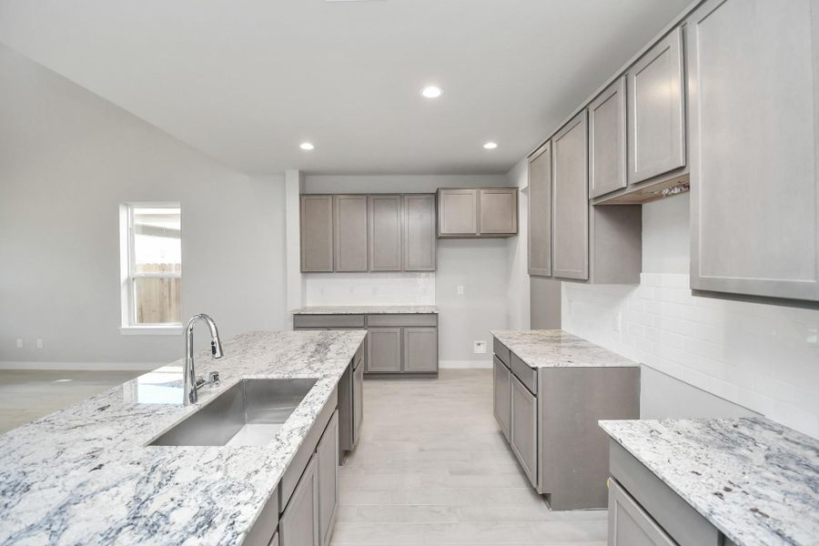 Step into a dream realized with this generously spacious kitchen! A massive granite island takes center stage, complemented by high ceilings, soft-close cabinets, granite countertops, stainless steel appliances, a sleek tile backsplash, and recessed lighting. Sample photo of completed home with similar floor plan. Actual colors and selections may vary.