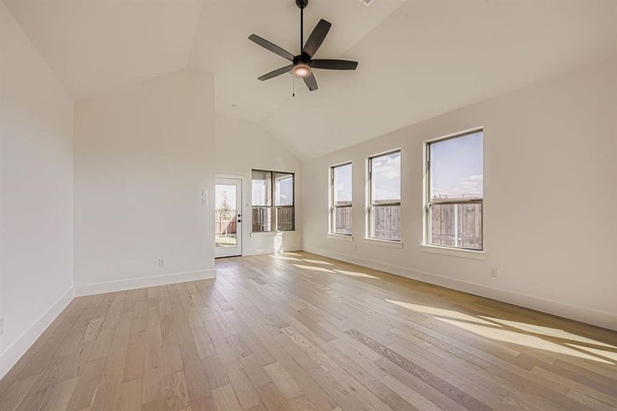 Empty room with light wood finished floors, high vaulted ceiling, and a ceiling fan Empty room with light wood finished floors, high vaulted ceiling, and a ceiling fan