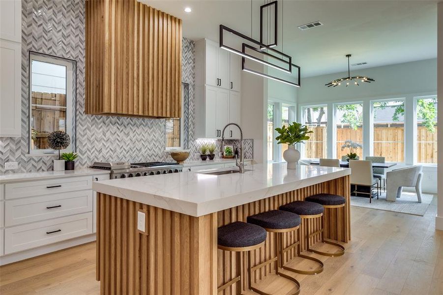 Kitchen featuring backsplash, light wood-type flooring, light stone counters, sink, and a center island with sink