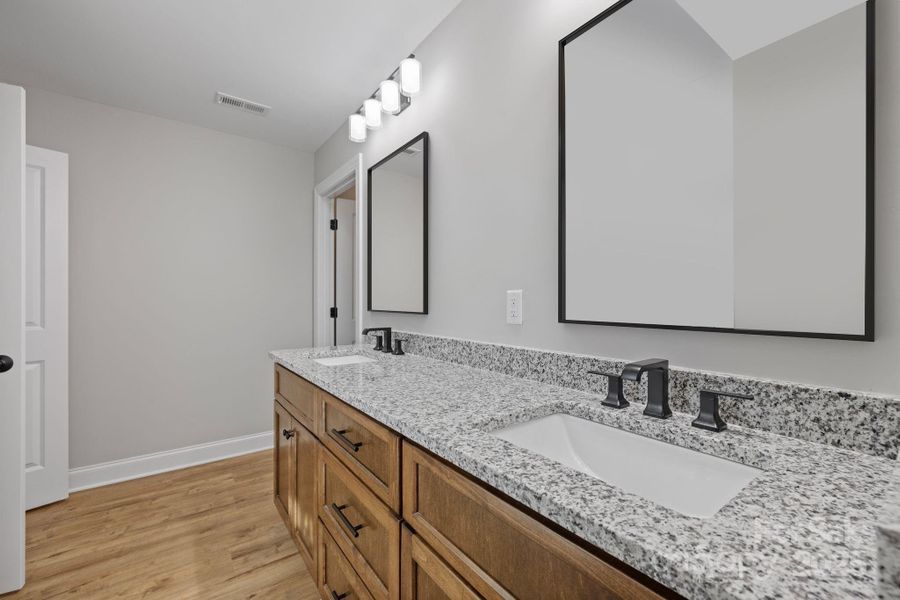 Primary bathroom features a spacious double vanity with custom wood cabinetry, granite countertops, sleek black fixtures, and modern framed mirrors. Primary bathroom features a spacious double vanity with custom wood cabinetry, granite countertops, sleek black fixtures, and modern framed mirrors.