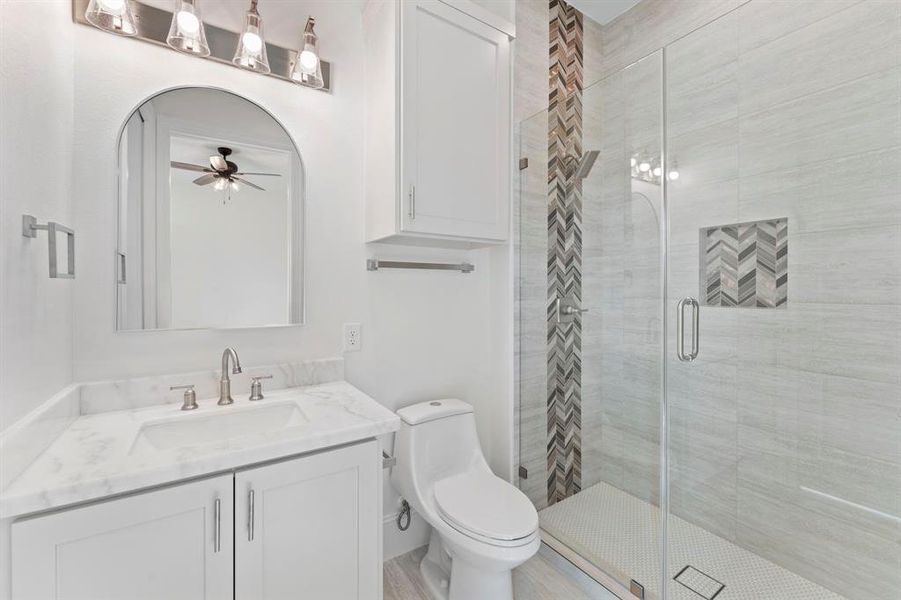 Premium level finishes in every bathroom. This ensuite has Calacatta Lada marble counters, an arched mirror, shampoo niche, and a glass-enclosed walk-in shower with stylish herringbone tile accents.