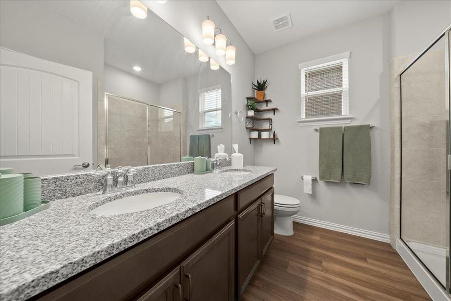 Full Bathroom located next to Bedroom 1 featuring hardwood / wood-style floors, vanity, toilet, and walk in shower.