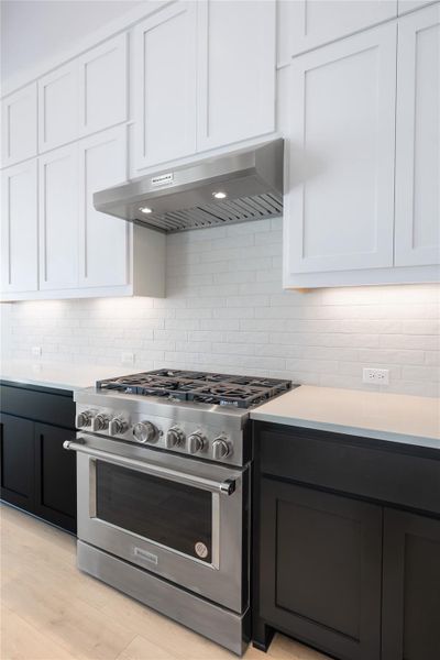 Dual tone kitchen featuring dual tone cabinets, stainless steel range, tasteful backsplash, and light stone counters