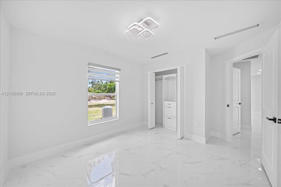 White tile flooring, modern ceiling light fixture, built-in closet storage, window with privacy blind, white panel doors White tile flooring, modern ceiling light fixture, built-in closet storage, window with privacy blind, white panel doors