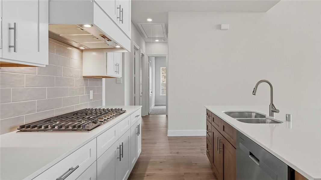 Contemporary kitchen featuring a gas range, subway tile backsplash, white shaker cabinetry with brushed nickel hardware, a kitchen island with a double basin sink, and wood-finish flooring
