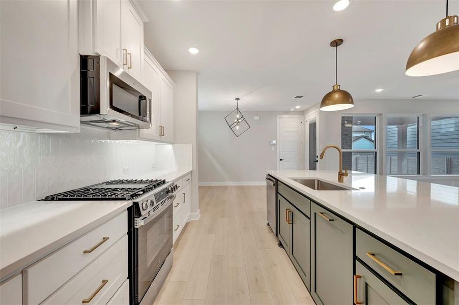 Two tone kitchen with stainless steel appliances, dual tone cabinets, pendant lighting, light wood finished floors, and light stone countertops
