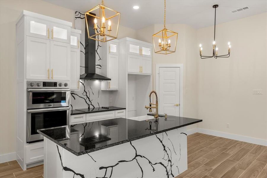 Kitchen with an island with sink, white cabinetry, wood tiled floors, double oven, and glass insert cabinets