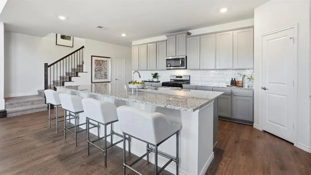 Kitchen with gray cabinetry, a kitchen bar, light stone counters, a center island with sink, and recessed lighting